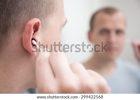 close up of young man cleaning his ear with a cotton swab