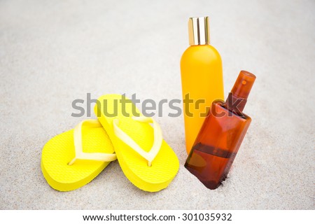 skin care concept - flip flops and suntan lotion bottles in sand on the beach