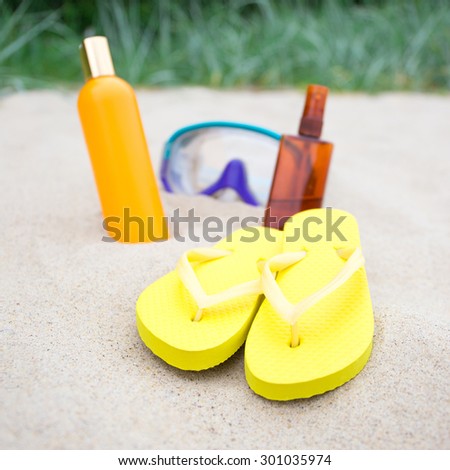 beach concept - close up of flip flops, suntan lotion bottles and diving mask on the sand