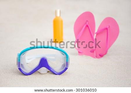 summer background - diving mask, flip flops and suntan lotion bottle on sandy beach