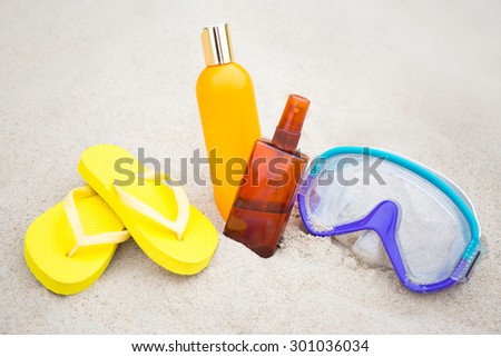 summer concept - flip flops, suntan lotion bottles and diving mask in sand on the beach