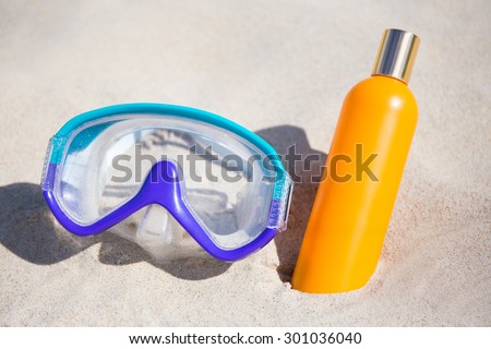close up of diving mask and suntan lotion bottle on sandy beach