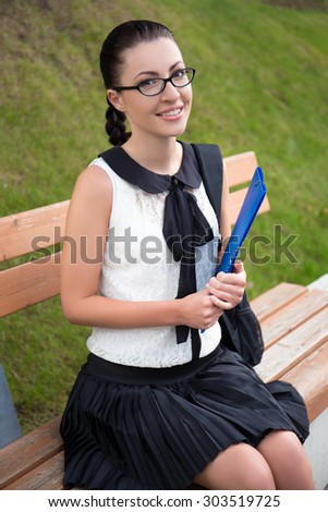 portrait of beautiful school girl or student sitting on bench in summer park