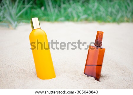 summer and skin care concept - suntan lotion and spray bottles on sandy beach