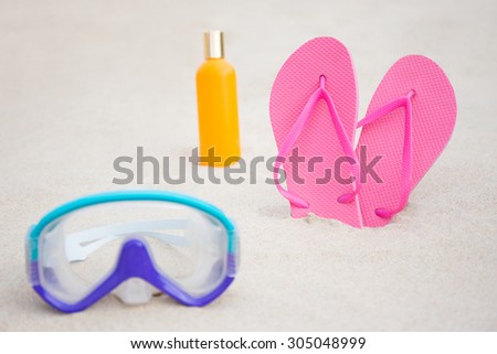 close up of diving mask, pink flip flops and suntan lotion bottle on sandy beach