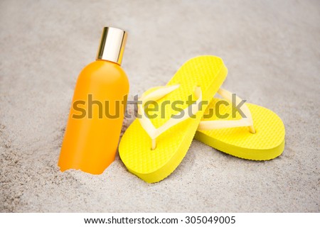 summer and skin care concept - yellow slippers and suntan lotion bottle on sandy beach