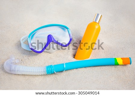 summer concept - close up of diving mask and suntan lotion bottle on sandy beach