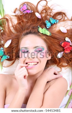 young redhead woman with butterflies and petals on her head lying biting her finger