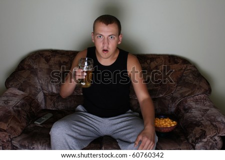 young interested man watching tv with beer and chips
