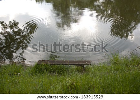 Peaceful landscape, a bench by the lake and a large water ring on the water surface