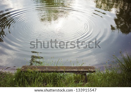 Peaceful landscape, a bench by the lake and a large water ring on the water surface