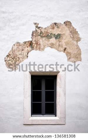 Little old white window with white stone frame on peeled plaster white wall