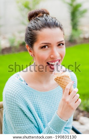 Young brown haired happy girl eating cold sweet ice cream  in mint green sweater on a bright summer day on green grass garden background