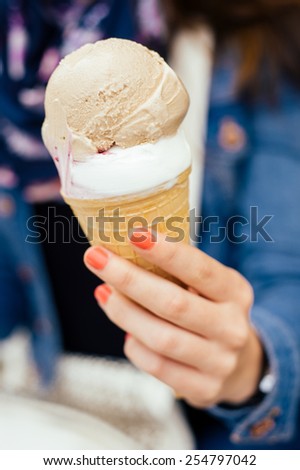 Cold titbit sweet hazelnut and vanilla ice cream scoops in crispy cone in red nailed young womans hand