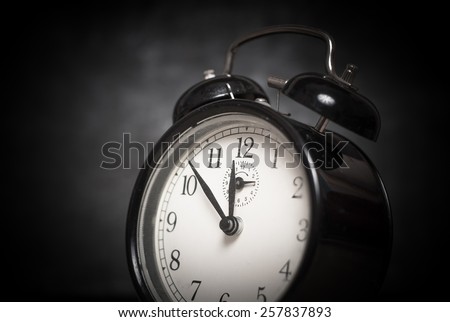 Old style vintage black metal alarm clock shows the time on dark gray background, close up image