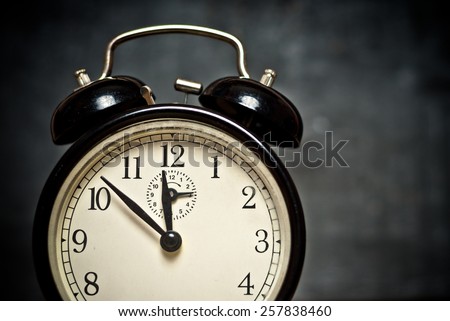 Old style vintage beige brown faced black metal alarm clock shows the time on dark gray background, close up image