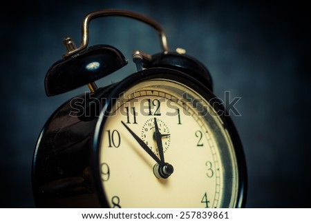Old style vintage black metal alarm clock on dark blue background, close up vintage acid colored image