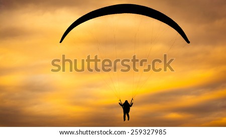 Black silhouette of paragliding man on the cloudy orange summer sunset