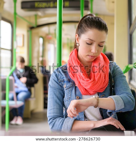Young brown haired trendy woman looks at her watch while waiting to start the tram