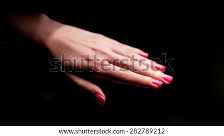 Decorative girly pink painted nails on pretty young woman hands on isolated black backround