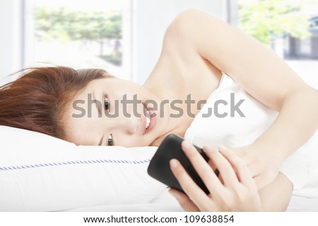 smiling young woman looking smart phone on the bed