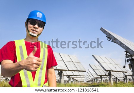 happy worker with thumb up and standing before solar panel tracking system