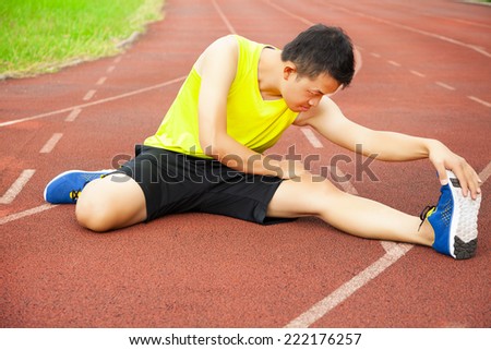 young man sitting on the track and stretching his leg to warm up