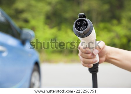 hand holding plug in connector for Charging electric car. eco energy concept