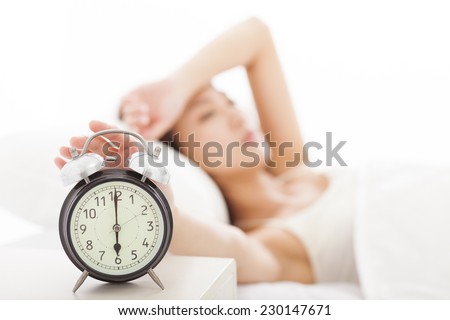 young Woman turning off the alarm clock on the bed