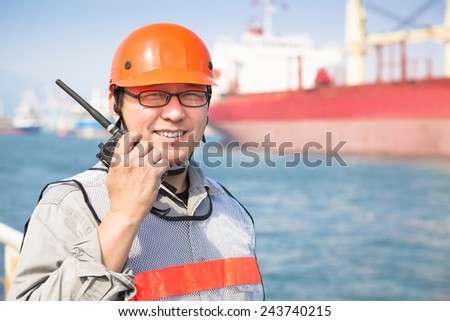 smiling dock worker holding  radio and  ship background