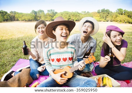 happy young friends enjoying picnic and playing ukulele