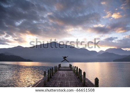 Successful businessman jumping on the pier and watching sunrise and mountain