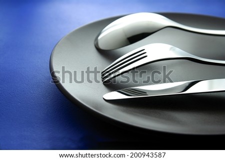 Spoon, fork, knife and plate Photo of a silver spoon, fork, table knife and a ceramic plate