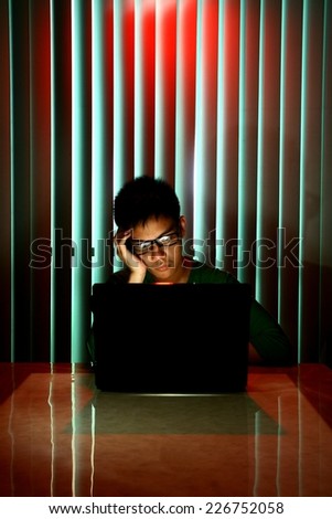 Young Teen with eyeglasses and bored in front of a laptop computer Photo of a Young Teen with eyeglasses and bored in front of a laptop computer