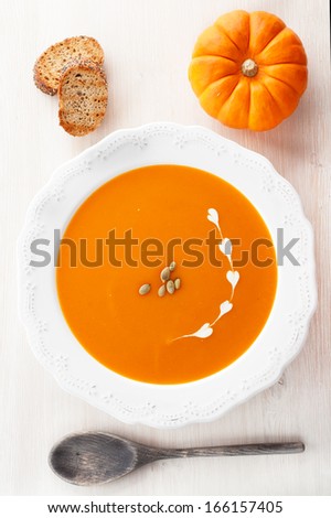 Plate of pumpkin soup with a wooden spoon on a light background