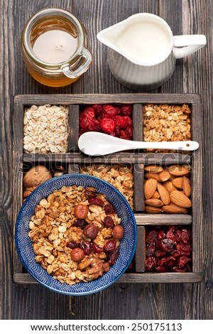 Wooden box with breakfast items - oats, granola muesli, nuts, honey, dried berries and milk. Top view.