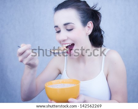 Portrait of a beautiful young woman eating a healthy bowl of cereal with strawberries