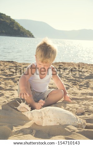 Cute little boy playing with shells in the beach.