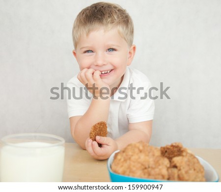 Cute little boy is having a breakfast. Child eating cookies and drinking milk.