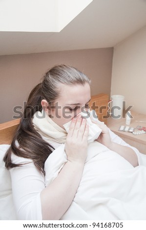 Sick young woman blows her nose into a tissue