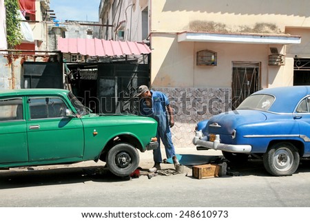 HAVANA, CUBA - APRIL 6, 2014: Cuban man making repairs to an old car on the street.