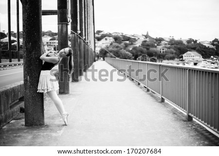 A beautiful blonde lady is standing on top of a bridge leaning against one of the pillars. It isa  black and white photo.