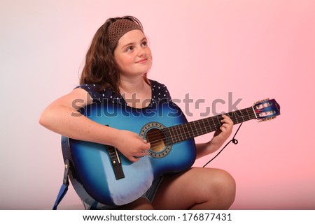 A pretty young brunette girl is playing a blue guitar in studio.