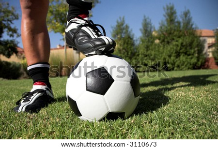 Man standing with his foot/ soccer boot on the soccer ball in his back yard.