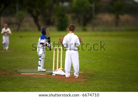 nine year old boys playing cricket, bowler running in but keeper is not focused on the game.