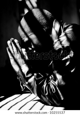 Young man praying for the safety of his country, Zimbabwe. Kneeling down, hands together.