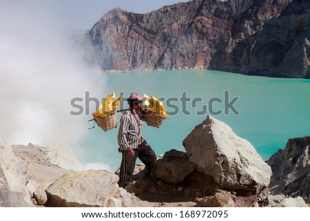 Kawah Ijen, Indonesia - August 11: Worker Carries A Basket With Pieces Of Sulfur On His Shoulder On August 11, 2013. Miners Each Carry Up To 90kg Of Sulfur Up Steep Cliffs At Kawah Ijen Volcano.