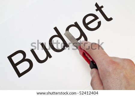 A hand cutting the word budget with a stanley knife