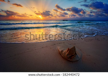 Peaceful sunrise with god rays over pristine sandy beach with a sand sculpture in the foreground