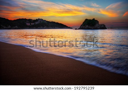 Peaceful sea bay sunrise over a sandy beach with orange clouds and distant cliffs